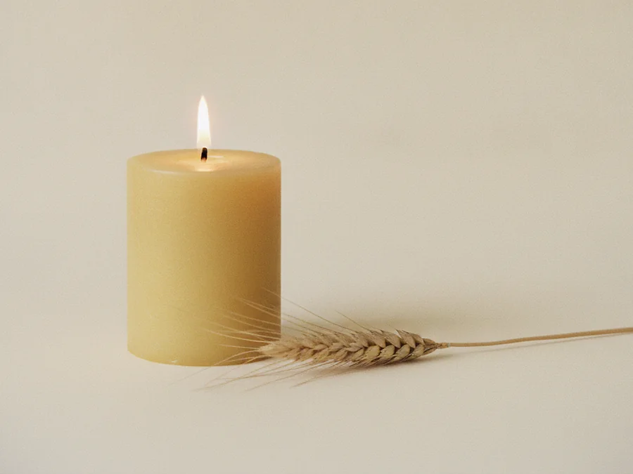 Vela amarilla encendida con una espiga de trigo a su lado