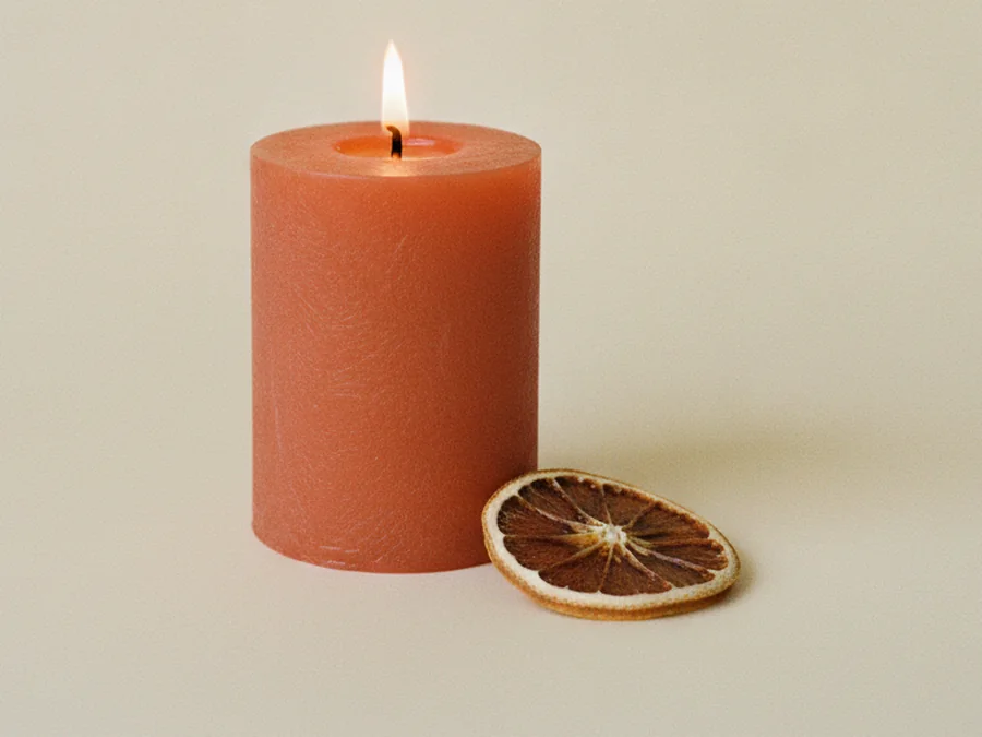 Vela naranja encendida con una rodaja de naranja seca a su lado