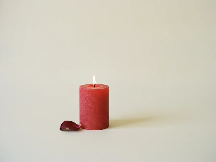 Vela roja encendida con un pétalo de rosa seco a su lado