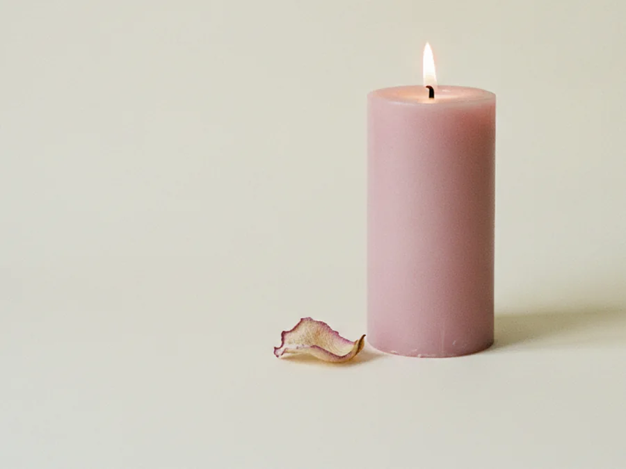 Vela rosa encendida con un pétalo de rosa seco a su lado