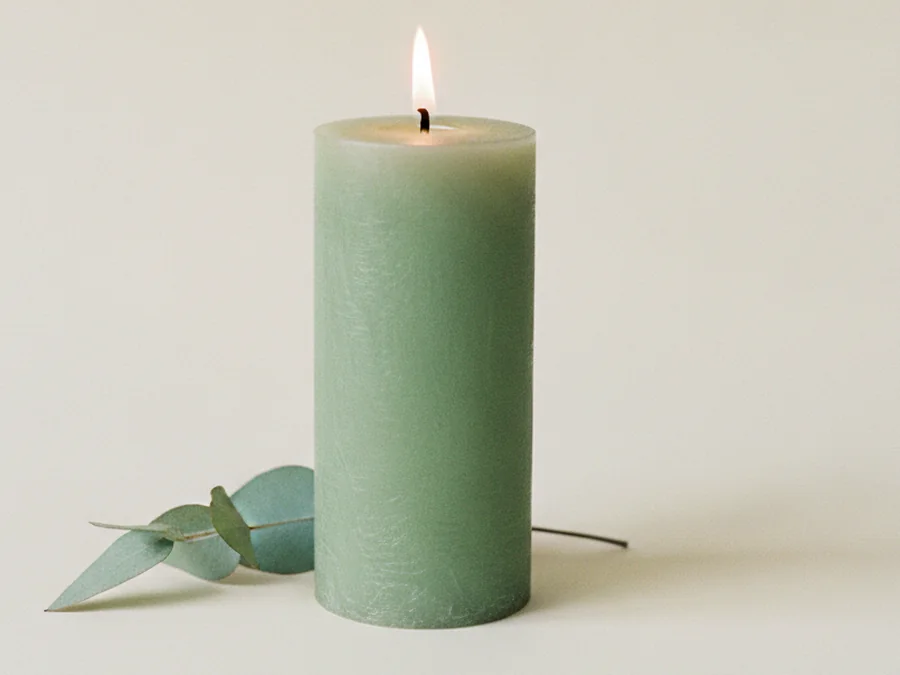 Vela verde encendida con una hoja de eucalipto a su lado