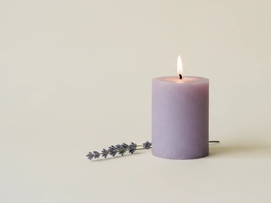 Vela violeta encendida con una rama de lavanda a su lado